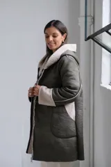 Tapado de corte recto con capucha, confeccionado en material tipo cuero con interior de corderito sintético. Presenta cierre frontal, bolsillos laterales y puños con vuelta de corderito.