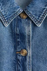 Campera camisera en denim rígido con cuello, cierre frontal de botones, puños abotonados, bolsillos de parche delanteros y dobladillo redondeado.