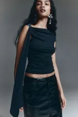 Top negro de punto elástico con escote asimétrico de un hombro, detalle de metal plateado y tira larga. Diseño entallado con laterales fruncidos para crear un efecto drapeado.