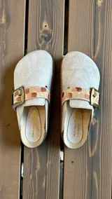 Sandalias de cuero blancas modelo Saki, estilo zueco, con hebilla metálica ajustable y detalle de diseño pintado a mano en la tira.
