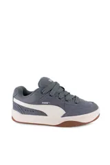 Championes Puma modelo Park Lifestyle Sk8, de diseño urbano inspirados en el skate, color blanco con franja lateral negra, detalles en gamuza gris en la puntera y suela de goma marrón tipo gum.