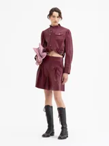 Short de cuero color vino tinto con tablas que generan volumen en las piernas, cintura doble con pespunte y botones forrados en cuero. Cierre lateral.