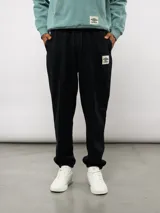 Pantalón de felpa negro con cordón ajustable en la cintura, costuras verticales en la parte delantera y etiqueta con el logo de Umbro en el muslo izquierdo.