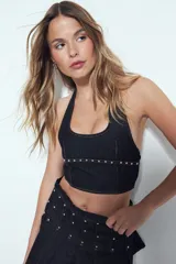 Top halter de denim oscuro, ajustado al cuerpo, con escote redondeado y una tira horizontal decorada con tachas plateadas a la altura del bajo.