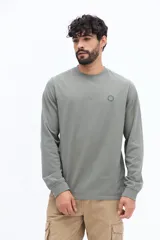 Remera de manga larga color blanco roto o gris muy claro, con escote redondo y un pequeño logo circular estampado en el pecho.