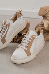 Championes de cuero con diseño de paneles en color blanco y tostado. Presentan suela de plataforma, cordones planos al tono y detalle de tirador en el talón.