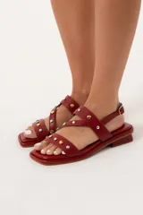 Sandalia baja color rojo de cuero con agarre trasero con hebilla y detalle de tachas de distintas medidas en la capellada.