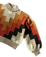 Buzo de tejido de punto con cuello alto y diseño geométrico en zigzag. Presenta una combinación de colores cálidos como naranja, rojo, negro y beige, con puños y cintura acanalados.