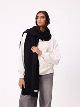 Bufanda de tejido de punto grueso en color negro, con etiqueta de la marca Rusty en uno de los extremos.