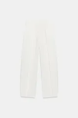 Pantalón blanco de tiro alto, con pliegues en el delantero, bolsillos laterales ocultos y cierre frontal con cremallera y ganchos metálicos.