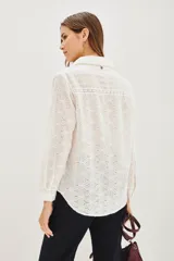 Camisa de manga larga en color blanco, confeccionada en tejido de algodón con diseño calado tipo broderie. Presenta cuello clásico, cierre frontal con botones y paneles frontales con tablas verticales.