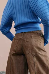 Jeans de tiro medio con diseño wide leg, confeccionados en denim color marrón con efecto lavado. Presentan cinco bolsillos, cierre frontal con cremallera y doble botón metálico.