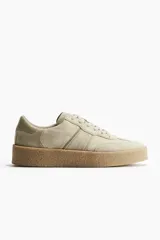 Zapatillas deportivas color beige con collarín acolchado, lengüeta y cierre de cordones. Suela texturizada gruesa con diseño.