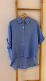 Camisa celeste de lino italiano, corte holgado, con cuello clásico, cierre frontal con botones de nácar y mangas cortas con puños arremangados.