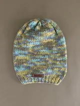 Gorro de lana tejido a mano de punto grueso, con diseño multicolor en tonos verde, celeste, amarillo y gris. Cuenta con una pequeña etiqueta de cuero sintético con el logo de la marca en el borde inferior.