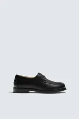 Zapato náutico de piel color negro con diseño liso, detalle de bordón en el empeine, horma cuadrada y suela con ligero tacón.