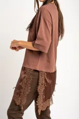 Remera oversize marrón con corte a la altura de la cadera, cuello redondo y mangas cortas holgadas. Incorpora un aplique inferior superpuesto de satén con detalles de encaje bordado en los bordes.