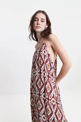 Vestido largo de silueta amplia y fluida, con breteles finos y escote redondeado. Presenta un diseño estampado con motivos geométricos en tonos bordó, beige y gris.