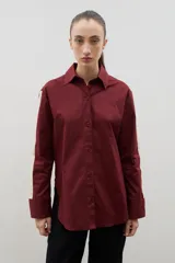 Camisa de corte holgado y largo medio, color negro con detalle de franja lateral en color crema a lo largo de las mangas. Presenta cuello clásico, cierre frontal con botones y tajos laterales en el ruedo.