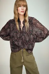 Blusa de manga larga con cuello redondo y escote en pico con lazada decorada con borlas. Confeccionada en tejido semitransparente con estampado paisley, cuenta con forro interior y cierre frontal con botones.