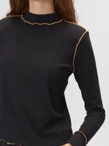 Polera de manga larga confeccionada en tela rib color bordó, con cuello alto y hombreras. Presenta costuras a la vista con pespuntes en hilo de color contrastante en el cuello, puños, hombros y ruedo.