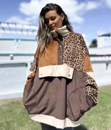 Buzo de estilo canguro con diseño de bloques de color y estampado animal print. Presenta una combinación de texturas en tonos marrón, chocolate y beige, con cuello alto, cierre frontal parcial con botones a presión y un bolsillo frontal grande con solapa.