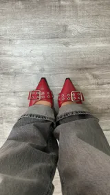 Stilettos rojos charol con punta fina, dos tiras con hebillas y detalles de tachas plateadas. Destalonados.