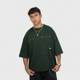 Remera de corte oversize color verde oscuro, con estampa gráfica en la espalda que incluye texto y diseño lineal.