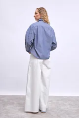 Camisa de mangas largas a rayas verticales azules y blancas, con cuello clásico y cierre frontal con botones. Presenta apliques de strass y ojalillos metálicos.