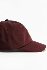 Gorra color borgoña de sarga de algodón con ojales bordados y correa ajustable con hebilla metálica en la parte trasera.