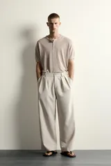 Pantalón relaxed fit de color blanco off-white, confeccionado en tejido con lino. Cuenta con pliegues frontales en la cintura, bolsillos delanteros y cierre frontal con cremallera y botón.