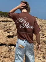 Remera celeste de corte holgado con estampado en la espalda que dice "Ittai Stars" en letras cursivas y "An Ibiza Produce" en mayúsculas.