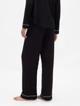 Pijama de dos piezas confeccionado en modal negro, compuesto por una camisa de manga larga con cuello solapa, cierre frontal de botones y vivos en contraste blanco, y un pantalón de corte recto con cintura elástica ajustable mediante cordón y vivos en el ruedo.