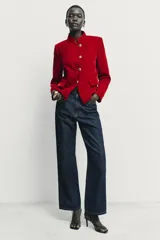 Blazer de terciopelo color rojo, con cuello subido, manga larga y cierre frontal cruzado con botones dorados. Presenta bolsillos delanteros con solapa.