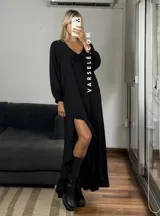 Vestido largo color marrón, con escote en V, mangas largas con puños y detalle de encaje en el pecho. Presenta un diseño asimétrico con volados en el ruedo y una abertura frontal.