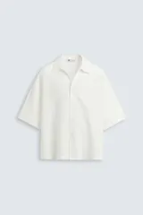 Camisa de corte relajado confeccionada en tejido fluido con mezcla de lyocell. Presenta cuello solapa, manga corta y cierre frontal con botonadura oculta.