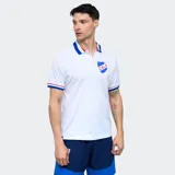 Remera tipo polo de fútbol del Club Nacional de Football, color blanco con cuello y puños en azul, blanco y rojo. Presenta el escudo del club en el pecho y logo de la marca.