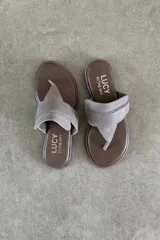 Ojota plana de cuero vacuno color marrón, de diseño tipo dedo con tira ancha en el empeine y detalle de aplique metálico con el logo de la marca.