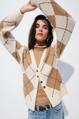 Saco tipo cárdigan de punto jacquard con diseño de rombos, escote en pico, cierre frontal con botones y hombros caídos. Presenta terminaciones acanaladas en cuello, puños y ruedo.