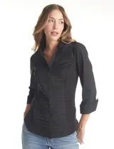 Camisa entallada de color negro con pechera estructurada mediante alforzas horizontales. Presenta cuello con solapa, escote en V, cierre frontal con botones y mangas tres cuartos con puños anchos rebatibles.
