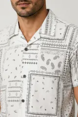 Camisa de manga corta color blanco con estampado tipo bandana en tonos grises, de corte holgado, con cuello camisero y cierre frontal de botones.