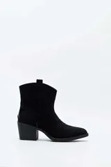 Bota corta de gamuza color negro, estilo texana, con taco cuadrado y puntera ligeramente perfilada. Presenta costuras decorativas en el empeine y tiradores laterales.