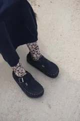 Zapatos tipo mocasín de cuero negro con diseño de tejido artesanal en el borde y cierre con hebilla metálica lateral. Presentan una suela plana de 2 cm.