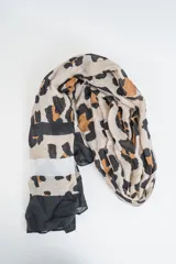Pañuelo grande de tela fina, con estampado de leopardo en tonos beige, negro y marrón, y bloques de color liso (negro y blanco) en los extremos.
