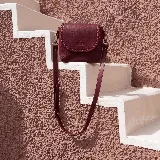 Mini cartera bandolera de cuero, de formato compacto y diseño atemporal con solapa frontal y costuras artesanales decorativas en el borde. Cuenta con el logotipo de la marca grabado en la parte delantera y correa larga regulable.