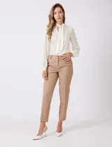 Pantalon de corte cigarette en color beige, confeccionado en tejido con apariencia denim y acabado satinado. Presenta tiro medio-alto, largo tobillero, cintura con presillas, cierre con gancho sastrero oculto, bolsillos laterales diagonales con botones forrados y pinzas traseras para un ajuste entallado.