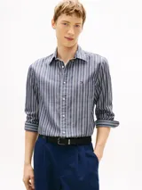 Camisa Tommy Hilfiger de corte regular, confeccionada en popelín de algodón azul con rayas verticales texturizadas. Presenta cuello camisero, cierre frontal de botones, mangas largas con puños abotonados y logo bordado en el pecho.