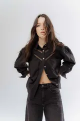Camisa negra de algodón con detalles de encaje broderie en el pecho y mangas. Presenta cuello clásico, cierre frontal con botones y mangas largas abullonadas.