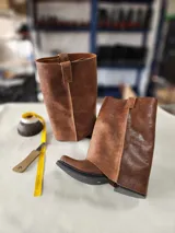 Bota de cuero marrón con diseño 2 en 1, que incluye una polaina desmontable. Presenta una caña alta estructurada y una base de bota tipo botineta con suela plana de goma negra.