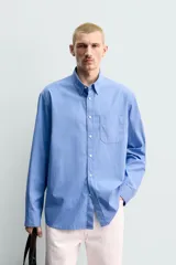 Camisa de corte regular fit confeccionada en tejido de algodón de color azul. Cuenta con cuello solapa, manga larga con puño abotonado, bolsillo de parche en el pecho y cierre frontal con botones.